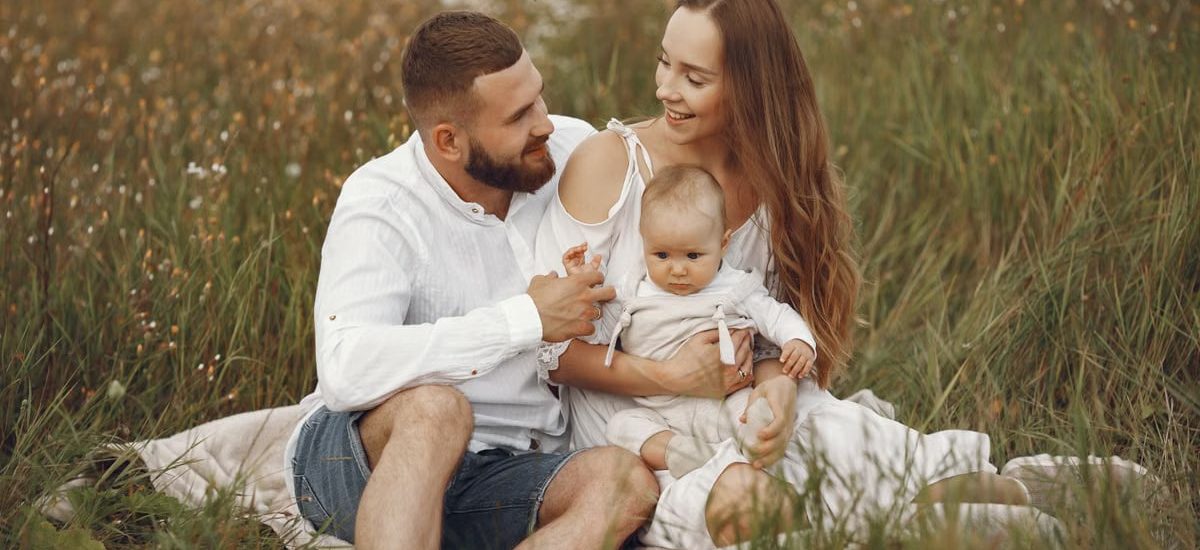 A joyful couple with their baby sitting on a blanket in a sunny meadow, embracing the beauty of summer.