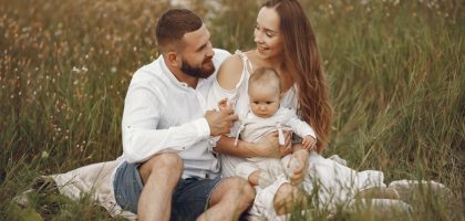 A joyful couple with their baby sitting on a blanket in a sunny meadow, embracing the beauty of summer.