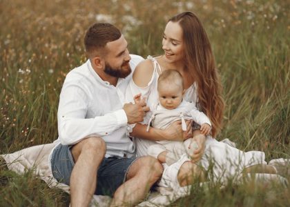 A joyful couple with their baby sitting on a blanket in a sunny meadow, embracing the beauty of summer.